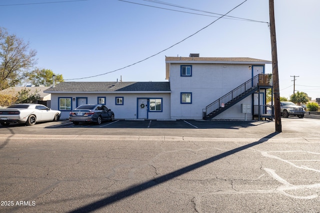 view of front facade featuring uncovered parking, stairway, and stucco siding