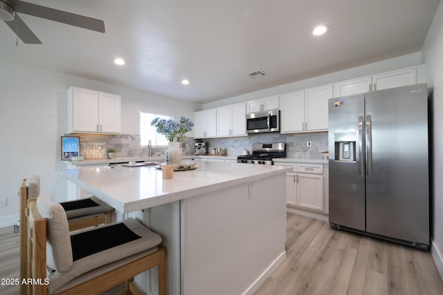 kitchen featuring a kitchen breakfast bar, stainless steel appliances, white cabinetry, and a center island