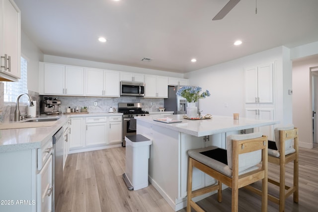 kitchen featuring white cabinets, light wood finished floors, appliances with stainless steel finishes, a center island, and tasteful backsplash