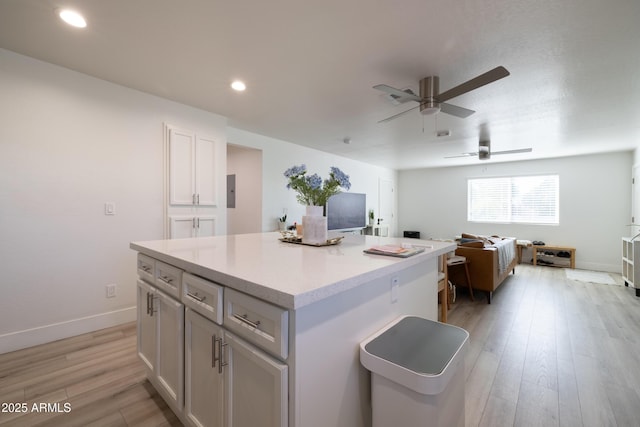 kitchen featuring baseboards, open floor plan, a center island, light countertops, and light wood-style floors