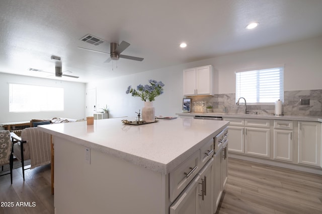 kitchen featuring light wood-type flooring, a center island, white cabinets, and a sink