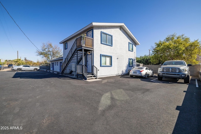 view of side of property with uncovered parking, stairway, and stucco siding