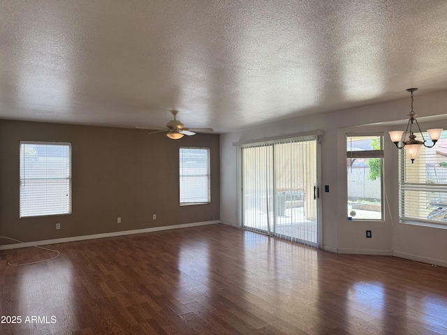 empty room featuring a textured ceiling, wood finished floors, ceiling fan with notable chandelier, and baseboards