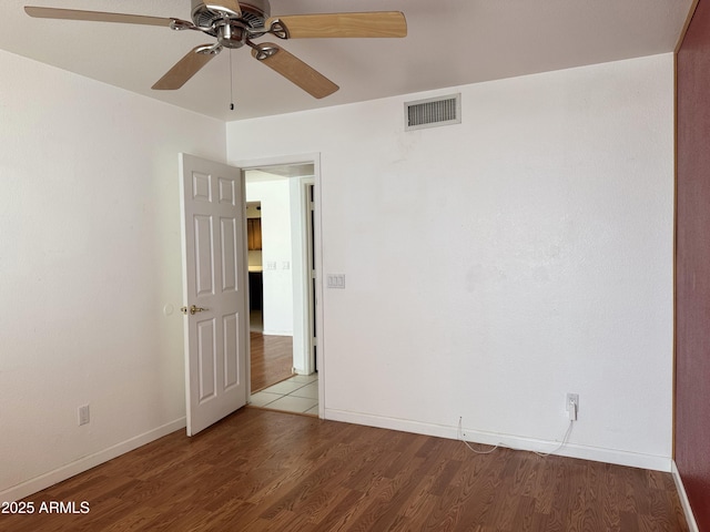 empty room with wood finished floors, ceiling fan, visible vents, and baseboards