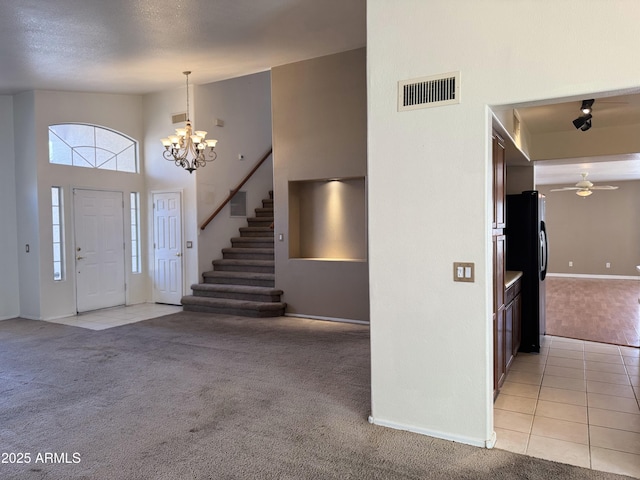 entrance foyer with stairs, ceiling fan with notable chandelier, light carpet, baseboards, and visible vents