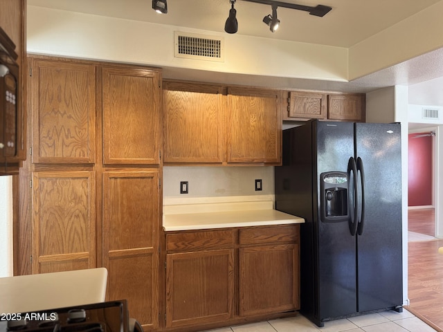 kitchen with visible vents, light tile patterned floors, black refrigerator with ice dispenser, and brown cabinets