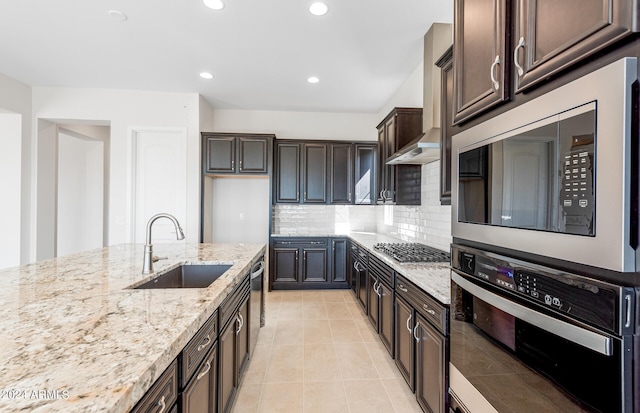 kitchen featuring tasteful backsplash, appliances with stainless steel finishes, light stone countertops, wall chimney exhaust hood, and sink