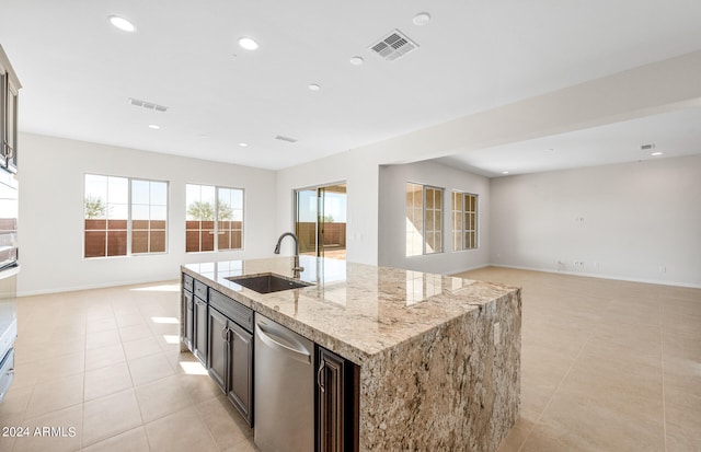 kitchen with sink, an island with sink, stainless steel dishwasher, light stone counters, and light tile patterned floors