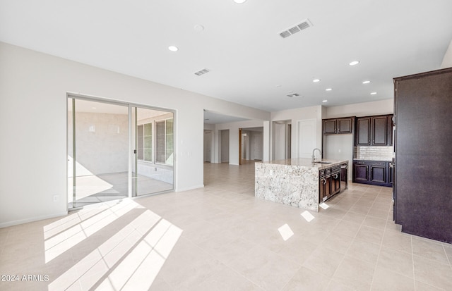 kitchen with dark brown cabinetry, a kitchen island with sink, sink, and light tile patterned floors