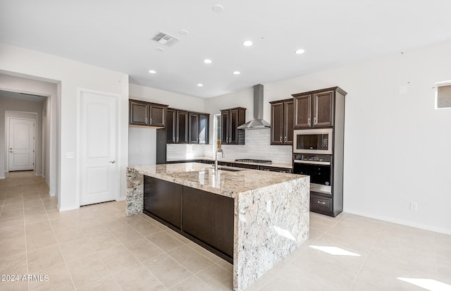 kitchen with a center island with sink, light stone counters, backsplash, wall chimney exhaust hood, and stainless steel appliances