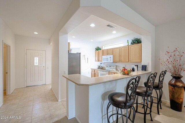 kitchen featuring a breakfast bar, kitchen peninsula, light tile patterned floors, and white appliances