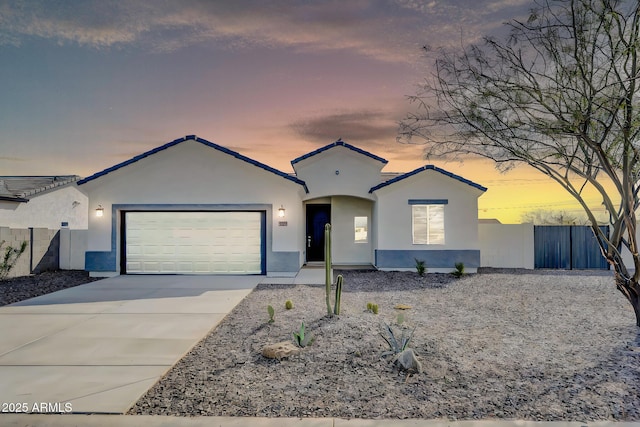 view of front of house with stucco siding, driveway, an attached garage, and fence