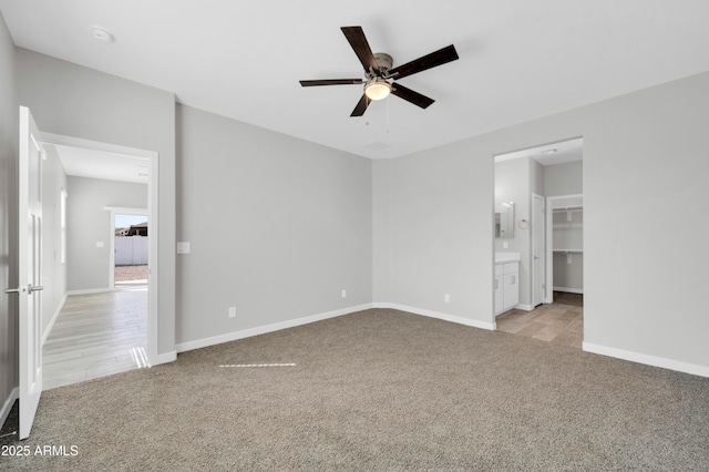 unfurnished bedroom with light carpet, a ceiling fan, a walk in closet, and baseboards