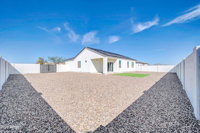 rear view of property with roof mounted solar panels, a patio, and a fenced backyard