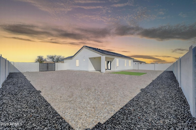 back of property at dusk with stucco siding, a gate, roof mounted solar panels, a fenced backyard, and a patio area