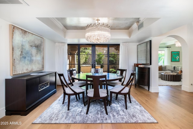 dining area with french doors, an inviting chandelier, crown molding, light wood-type flooring, and a tray ceiling