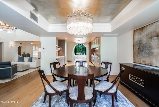 dining space featuring a notable chandelier, crown molding, wood-type flooring, and a raised ceiling