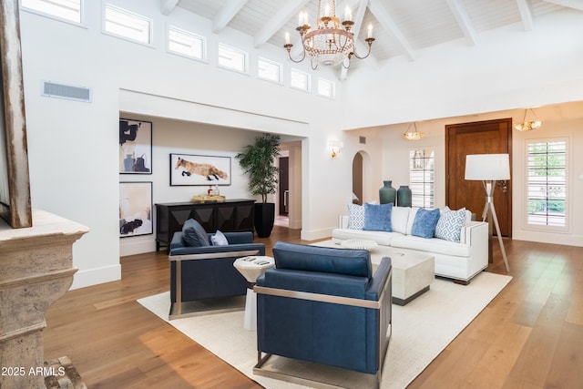 living room featuring beamed ceiling, high vaulted ceiling, a chandelier, and light hardwood / wood-style floors