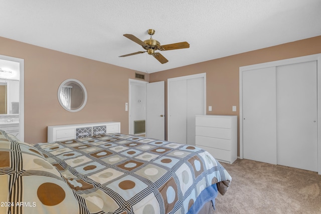 bedroom with ensuite bath, light colored carpet, a textured ceiling, two closets, and ceiling fan