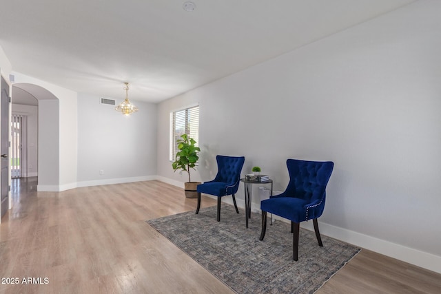 living area with arched walkways, light wood finished floors, baseboards, a notable chandelier, and visible vents