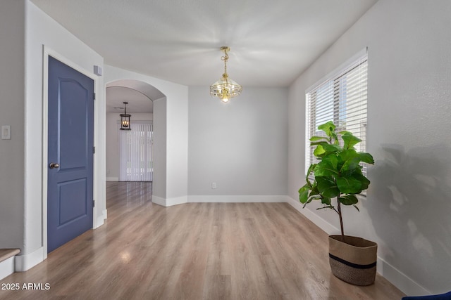 spare room with baseboards, arched walkways, and light wood-style floors