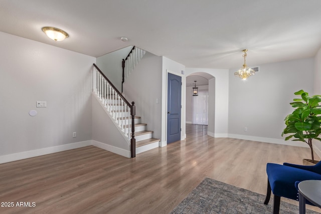 unfurnished living room featuring arched walkways, baseboards, an inviting chandelier, wood finished floors, and stairway