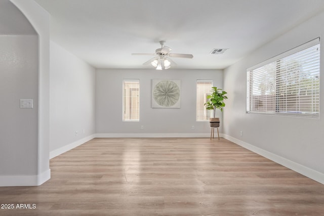 empty room featuring a ceiling fan, light wood finished floors, visible vents, and plenty of natural light