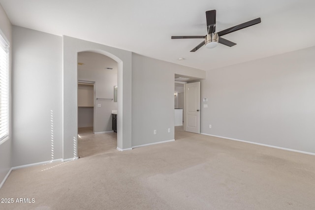 unfurnished bedroom with baseboards, arched walkways, a walk in closet, and multiple windows