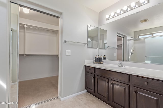 bathroom featuring a shower with door, visible vents, vanity, a walk in closet, and baseboards
