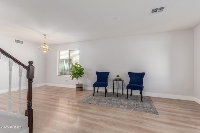 living area featuring a notable chandelier, wood finished floors, visible vents, and stairway