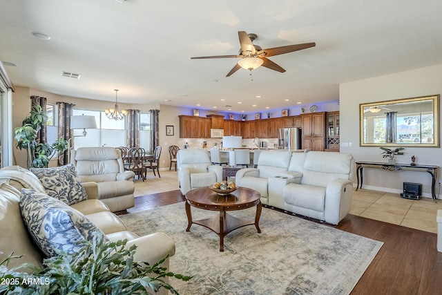 living room featuring light hardwood / wood-style floors, ceiling fan with notable chandelier, and a healthy amount of sunlight