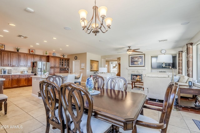 tiled dining room with a high end fireplace and ceiling fan with notable chandelier