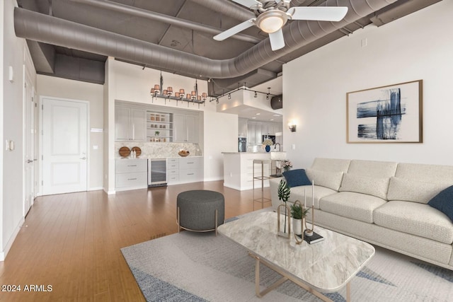 living room with rail lighting, wood-type flooring, beverage cooler, ceiling fan, and bar area