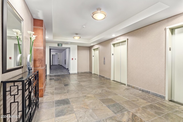 corridor with elevator and a raised ceiling