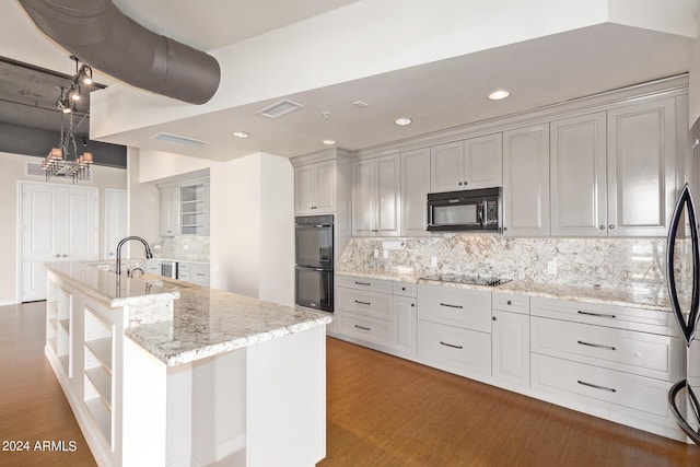 kitchen featuring tasteful backsplash, light stone countertops, an island with sink, and black appliances