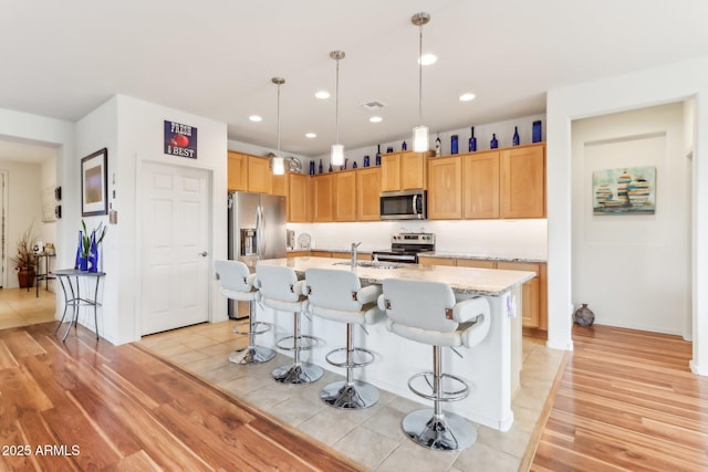 kitchen with light wood finished floors, a kitchen island with sink, a sink, appliances with stainless steel finishes, and a kitchen bar