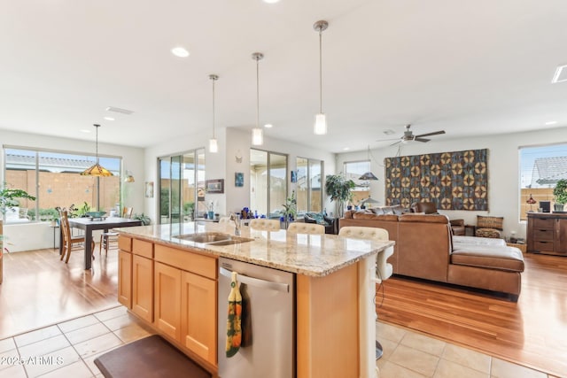 kitchen with dishwasher, an island with sink, light stone counters, light tile patterned flooring, and a sink