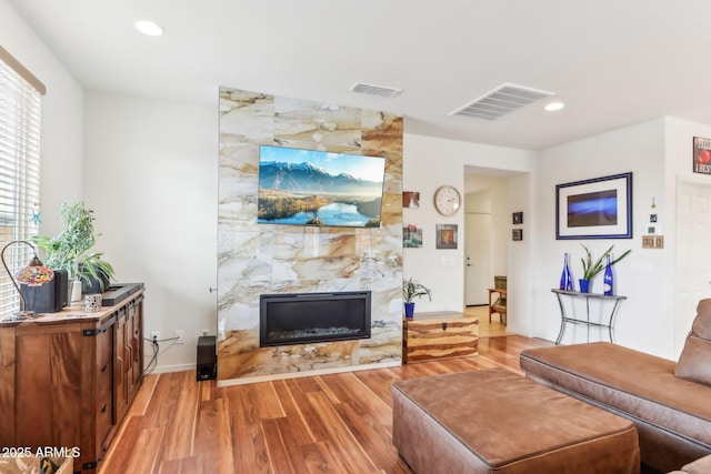 living room featuring recessed lighting, wood finished floors, visible vents, and a high end fireplace