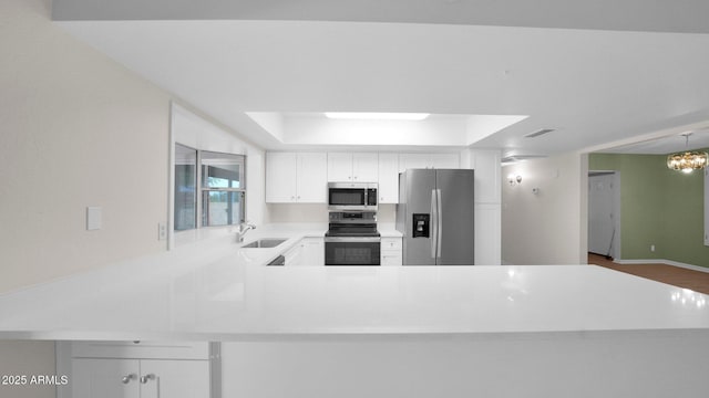 kitchen with light countertops, appliances with stainless steel finishes, white cabinets, a sink, and a peninsula