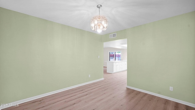 empty room featuring light wood finished floors, baseboards, visible vents, and a notable chandelier