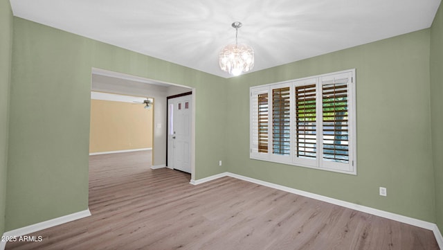 unfurnished room featuring ceiling fan with notable chandelier, light wood-type flooring, and baseboards