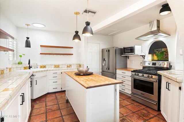 kitchen with white cabinetry, tile counters, a center island, stainless steel appliances, and extractor fan