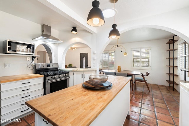 kitchen featuring wood counters, ventilation hood, decorative light fixtures, white cabinetry, and stainless steel appliances