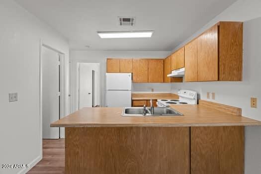 kitchen with sink, kitchen peninsula, wood-type flooring, and white appliances