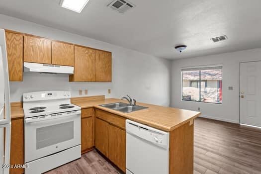 kitchen with sink, kitchen peninsula, hardwood / wood-style flooring, and white appliances