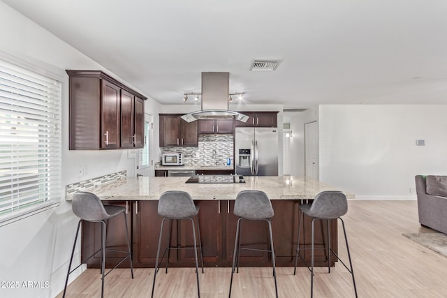 kitchen with tasteful backsplash, light stone counters, stainless steel refrigerator with ice dispenser, island range hood, and light wood-type flooring