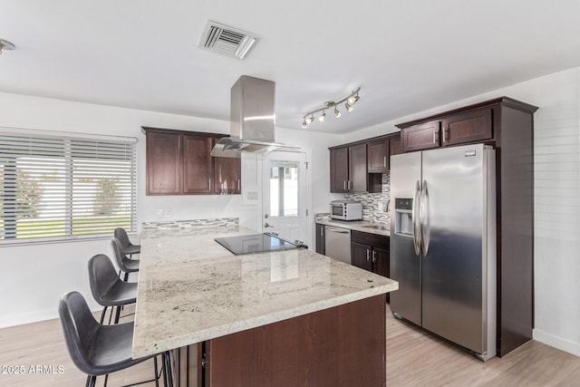 kitchen featuring stainless steel appliances, tasteful backsplash, light stone counters, island exhaust hood, and a breakfast bar