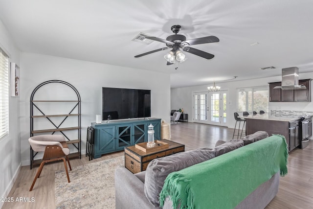 living room with ceiling fan with notable chandelier, light hardwood / wood-style floors, and french doors