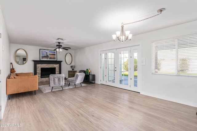 living room with a stone fireplace, french doors, ceiling fan with notable chandelier, and light wood-type flooring