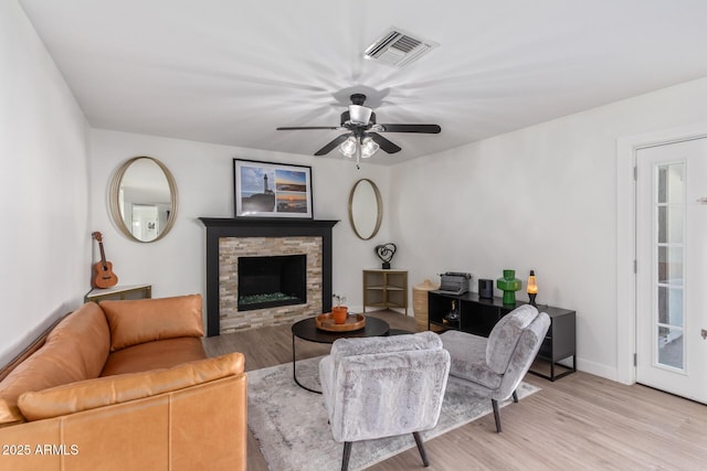 living room with a stone fireplace, ceiling fan, and light hardwood / wood-style floors